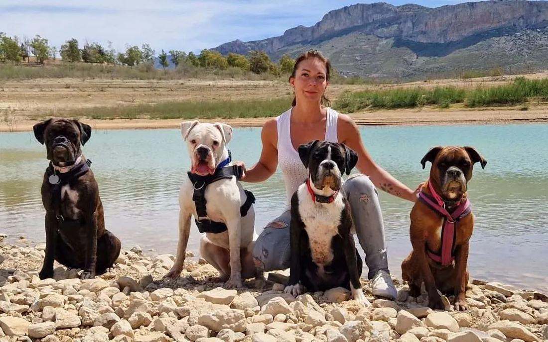 Justyna sitting on a pebbly lake shore with four Boxers